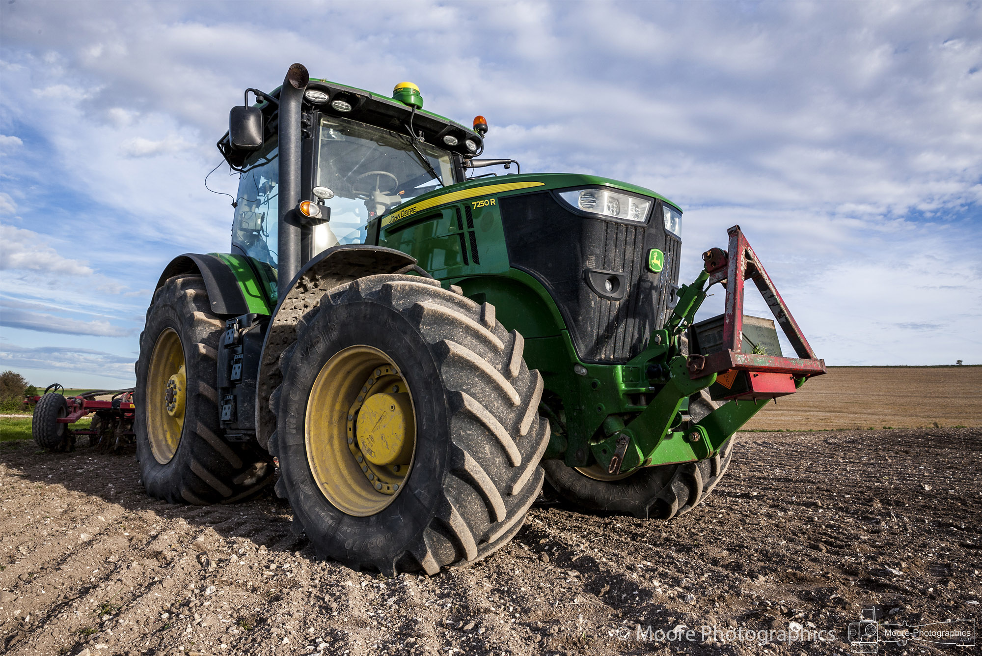 John Deere 7250R tractor with a cultivator standing on a ploughed chalk field under a broken sky